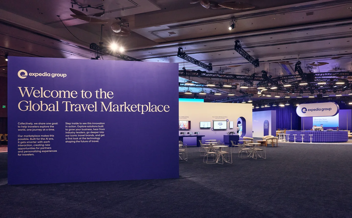 The Explore event hall: a purple Expedia Group wall reading “Welcome to the Global Travel Marketplace” in front of lounge seating and branded booths.